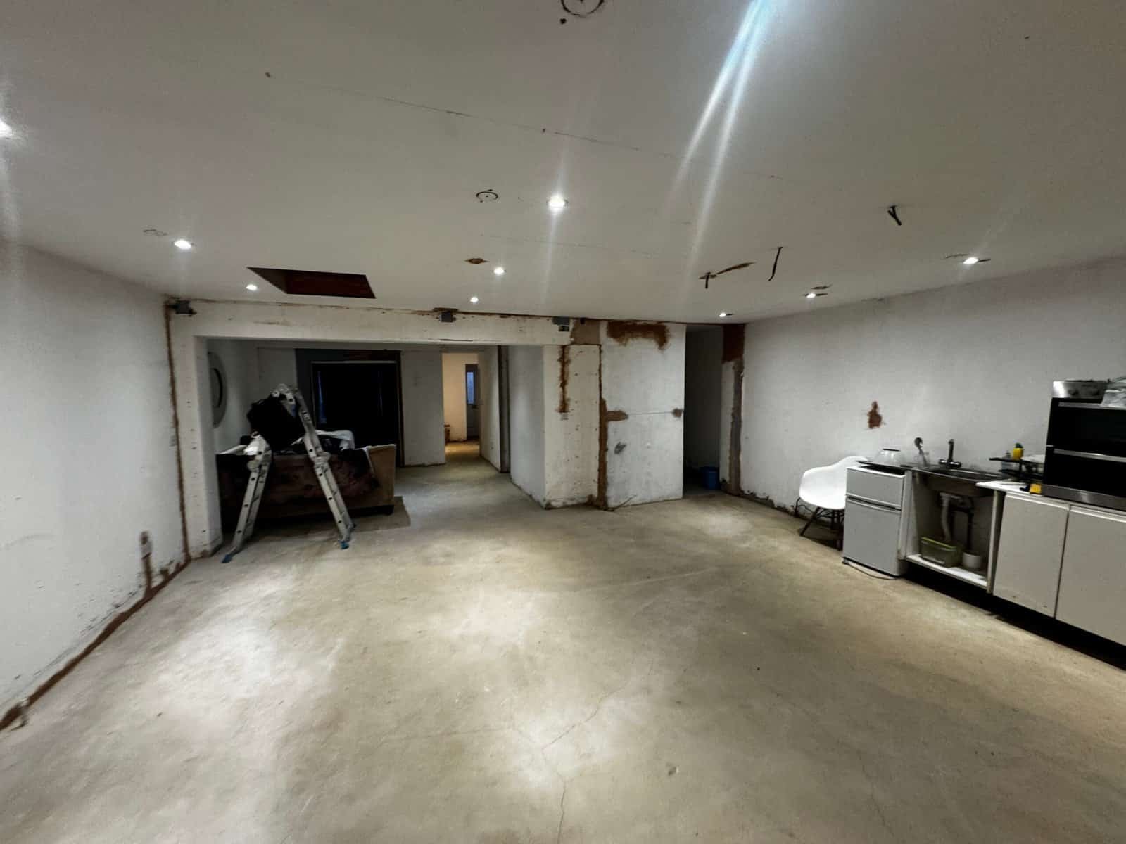 Gutted open-plan room in Greenford with water-stained ceiling, cracks and rust staining around the structural steelwork, left unfinished with a bare concrete floor