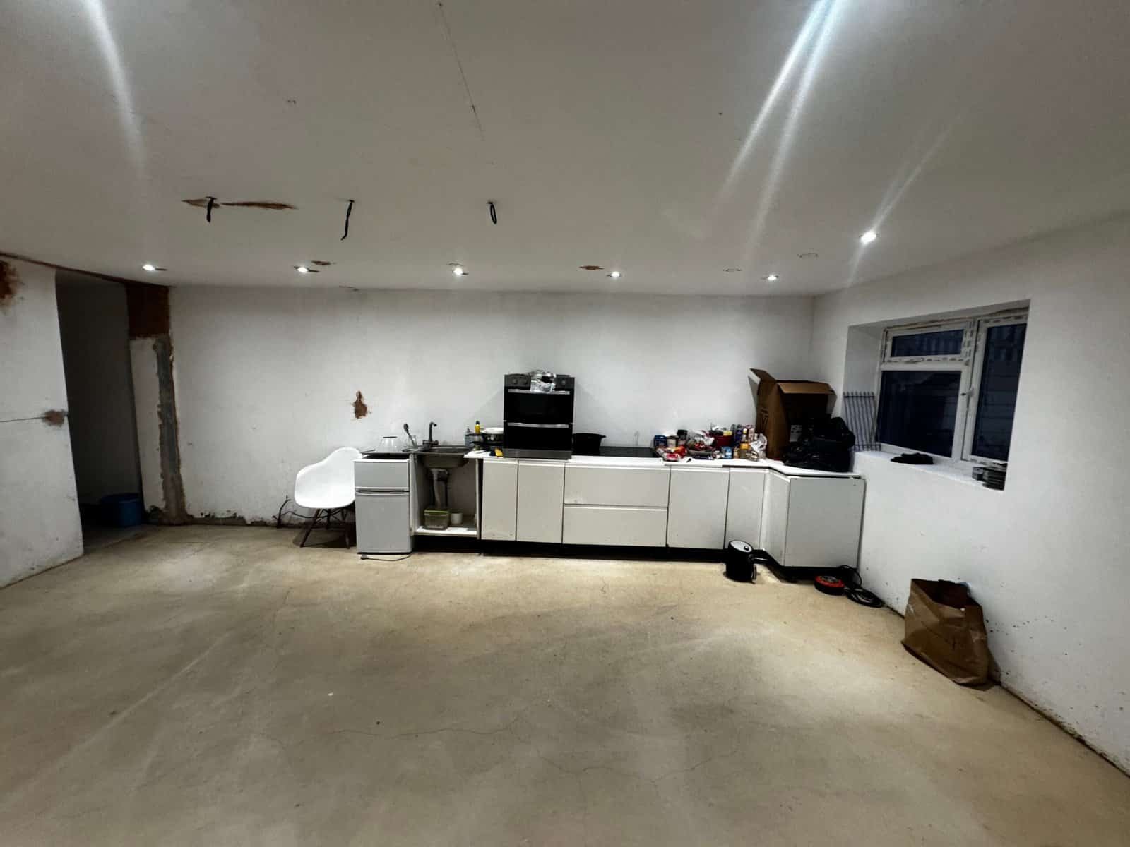 Makeshift kitchen of mismatched units in an unfinished Greenford room, with a damp-stained ceiling and damaged plaster walls