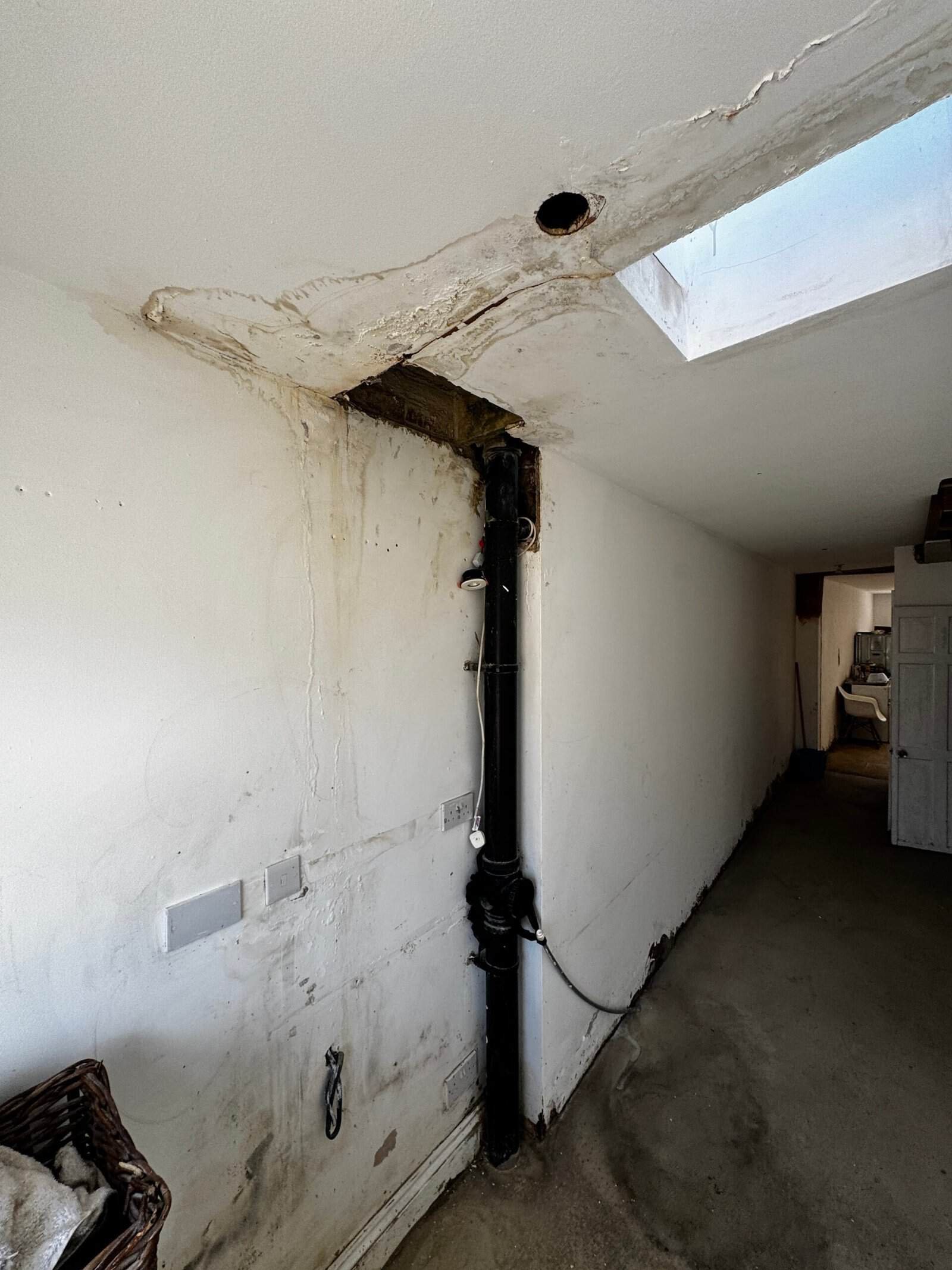 Interior ceiling and wall in a Greenford home with heavy water staining, blistered paint and damp tracking down beside a soil pipe